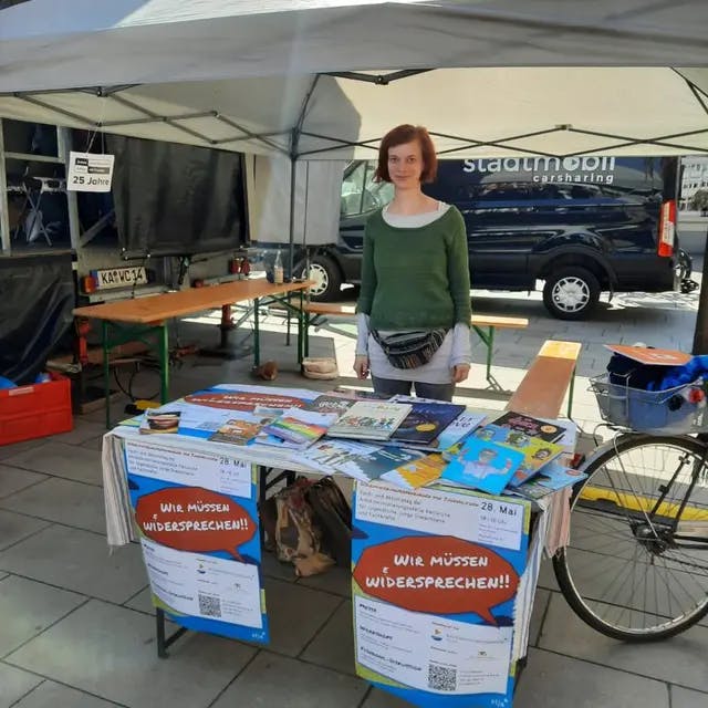 Abgebildet ist unser Stand auf dem Marktplatz mit vielen Broschüren und einer Mitarbeiterin der Antidsikriminierungsstelle Karlsruhe.